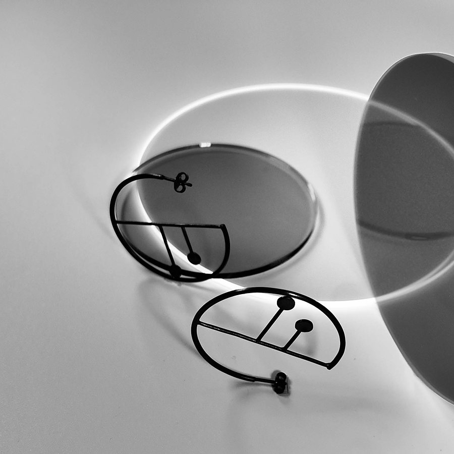 Black wire hoop earrings with a drawn line and two dots, beside translucent discs, black and white photo
