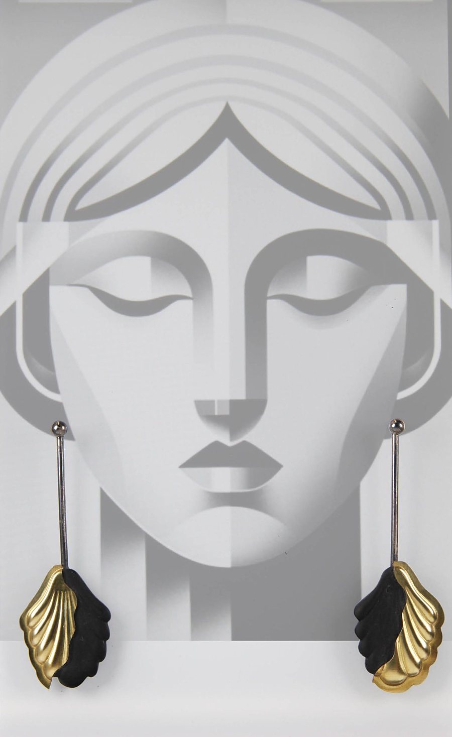 Earrings with a brass leaf and a matte black acrylic leaf on a long oxidized silver bar, in front of an art deco face illustration