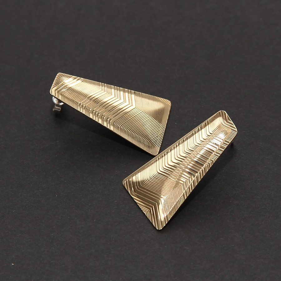 Brass trapezoid stud earrings with guilloché lines, seen from the side